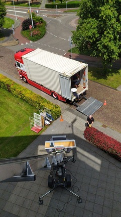 Een verhuiswagen met verhuislift wordt ingezet bij een verhuizing in een woonwijk, gezien van bovenaf.