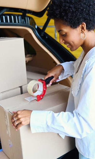 Vrouw pakt verhuisdozen in bij de open kofferbak van een auto in